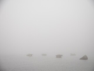 four small boats in the fog next to a rock.