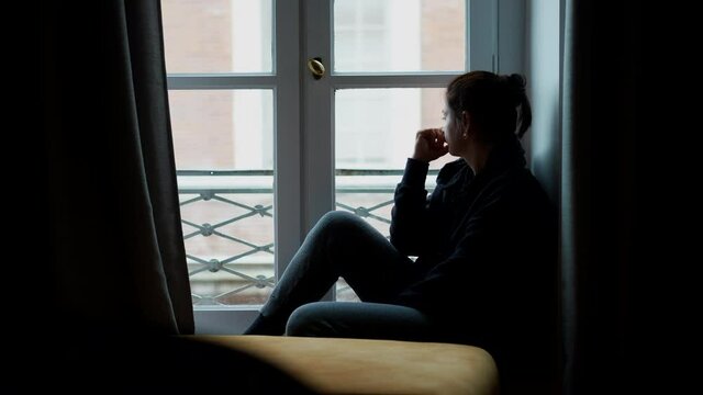 Woman sitting by apartment woman in melancholy. Pensive thoughtful person looking outside