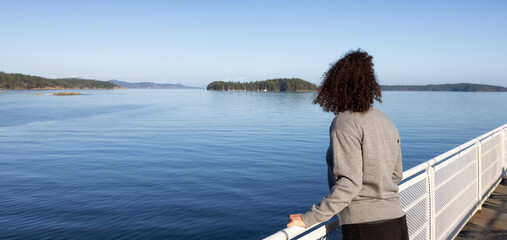Fototapeta premium White Caucasian Adult Woman watching the Canadian Nature Scenery from a ferry boat. West Coast of Pacific Ocean. Vancouver Island, British Columbia, Canada.