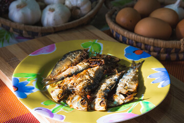 fried fish on a plate, brown eggs and garlic in shallow baskets in early morning light