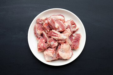 Raw pork ribs in white plate on dark background.