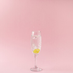 A champagne glass into which the grape fall making bubbles on pastel pink background. Minimal arrangement.