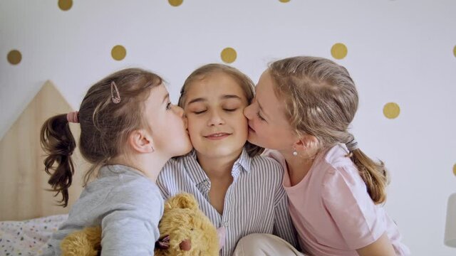 Front view of three girls sisters indoors at home, kissing.