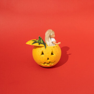 Halloween pumpkin from which a doll pops out on red background. Minimal scary concept.