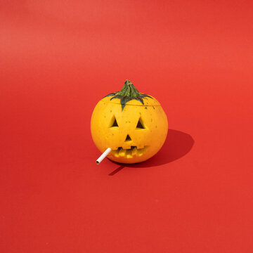 Halloween pumpkin with cigarette between  teeth on red background. Minimal art concept.