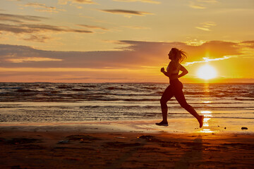 Fototapeta na wymiar Woman runs on sand near coast during sunset.