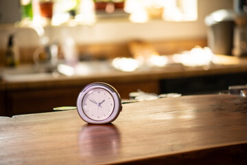 clock on wooden counter in kitchen with window and herbs in background