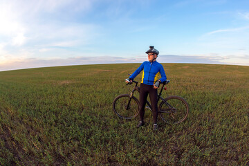 Obraz premium cyclist with a bicycle is resting on a green field against a blue sky. sports and recreation in nature