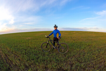 cyclist with a bicycle is resting on a green field against a blue sky. sports and recreation in nature