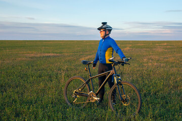 Fototapeta premium cyclist with a bicycle is resting on a green field against a blue sky. sports and recreation in nature
