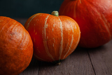 Three pumpkins in a row on wooden table in dark mood.