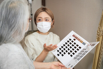 カラーサンプルで説明するマスク姿の美容師
