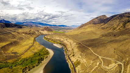 Aerial panoramic view of the Thompson river bending in its bed throughout a breathtaking mountainous landscape alongside Highway 1 in Thompson-Nicola Regional District, British Columbia, Canada
