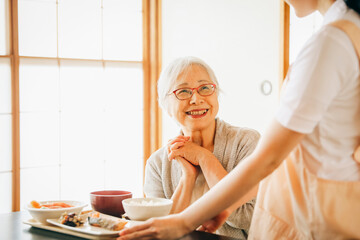 食事をする高齢者女性と女性スタッフ（配膳）
