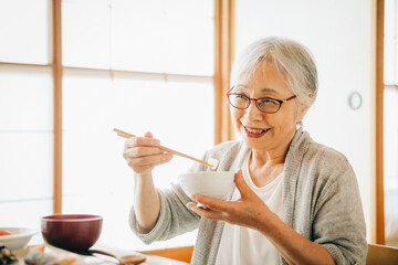 和室で食事を食べる高齢者女性（お米）
