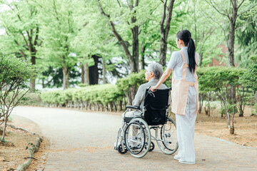 車椅子に乗った高齢者女性と女性スタッフ（後ろ姿・全身）
