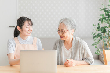 パソコンを使うエプロン姿の女性と高齢者（教える）
