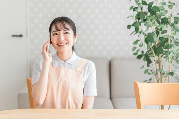 スマホで電話するエプロン姿の女性（笑顔）
