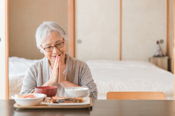 和室で食事を食べる高齢者女性（合掌）
