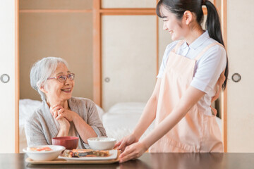 食事をする高齢者女性と女性スタッフ（配膳）
