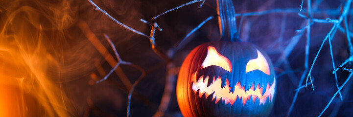 Spooky Halloween jack o lantern pumpkin with carved scary face glowing and billowing smoke in the...