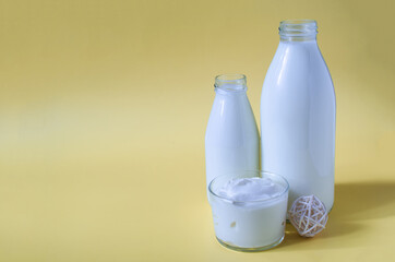 Sour cream in a glass container with milk bottles on a yellow background. Sour cream and dairy products in transparent dishes on a light background place for text