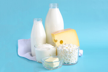 A set of milk products on a blue background close-up. Milk, kefir, sour cream, cheese, butter and cottage cheese in a glass container on a light background