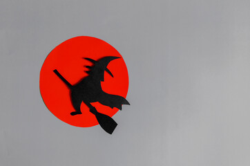 The shadow of a black witch flying on a broomstick against the background of a red moon. The layout...