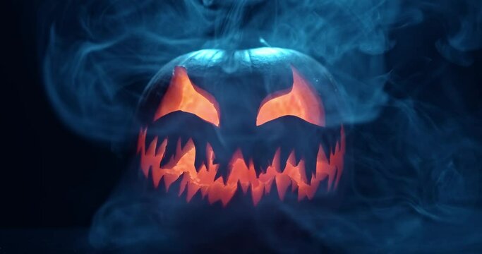 Spooky Halloween jack o lantern with glowing scary face carved out of a pumpkin and surrounded by smoke and mist.