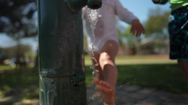 Child washing feet with park water faucet in sunny hot day