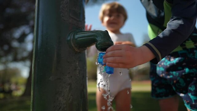 Child hands filling toy gun with water from public water faucet