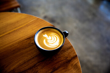 Fototapeta premium Cup of cappuccino with latte art on wooden background. Beautiful foam, wooden desk and bricks wall.