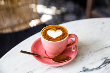 Trendy pink cup of hot cappuccino on marble table background. Heart shape latte art for symbol of love