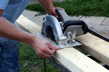 A man cuts wood planks with an electric saw.