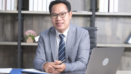 Portrait of senior asian businessman smiling and looking at camera while sitting at office,...