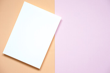 top view of vertical blank white paper card placed on light purple paper and old rose color paper background, flat lay.