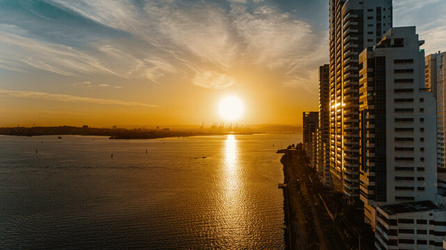 Hermoso amanecer atardecer sobre la bah&iacute;a con cielo naranja, amarillo y azul con edificios, gr&uacute;as y Sociedad Portuaria de fondo. Cartagena de Indias, Colombia