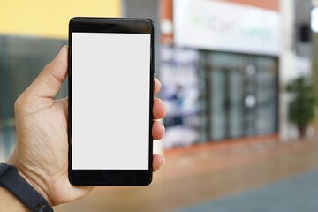 Adult hand holding a smartphone outside a store with blank copy space screen for text message or information content
