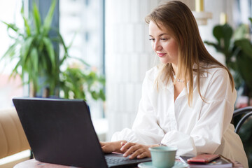 successful business woman sitting in cafe with laptop. work, communicates via Internet or e-leaning. office workplace with green plants.