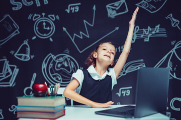 Caucasian emotional schoolgirl raises hand up sits at laptop during online lesson. Distant Learning.