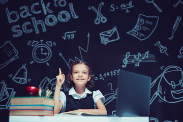 Smiling schoolgirl raising her index finger up. Sitting with laptop and books. Distance education 