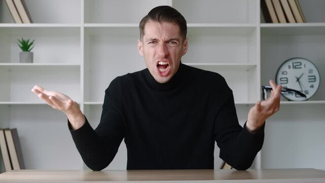 Shocked male businessman in white shirt takes off glasses and say what. Surprised and scared man looking to the camera while sitting at office interior background. Disagreement concept