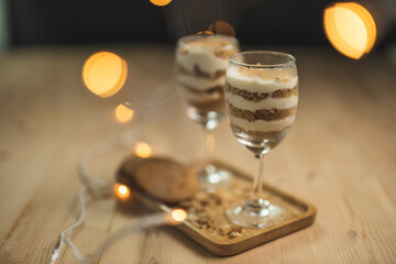 A wine glass fill with cream and crumb serve on a wooden plate with blurry background.