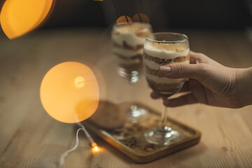 A wine glass fill with cream and crumb serve on a wooden plate with blurry background.