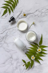 Fototapeta na wymiar Daily hygiene and female healthy skincare. Cosmetic cream and skin care serum with cammomile flofers on marble countertop. SPA organic beauty product. Top view flat lay. Copy space.