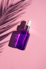 Purple glass dropper bottle with metallic lid. Top view on lilac background with eucalyptus leaves shadow. Skincare cosmetic. Beauty concept for face body care
