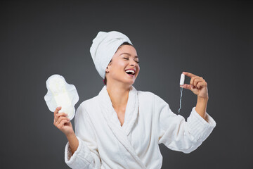 Tampon and sanitary napkin. A woman in a white bathrobe and towel wrapped around her head holds a...