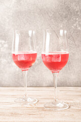 Two glasses of rose cocktails. Sparkling red cocktail with ice on wooden table made at home. Homemade red cocktails