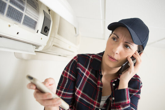 air conditioning engineer holding remote control and talking on smartphone