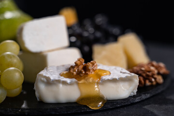 Baked camembert with apples dipped with honey and walnuts. Delicious appetizer. Close-up, dark background.